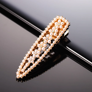 Close-up of golden duckbill hair clip with white pearls and light blue rhinestones
