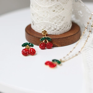 Detailed view of cherry jewelry set featuring red and green rhinestones on gold chain