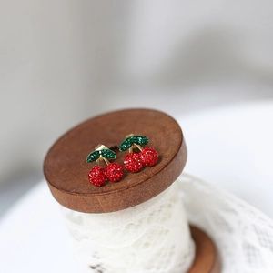 Detail of cherry stud earrings with red and green crystals on vintage lace