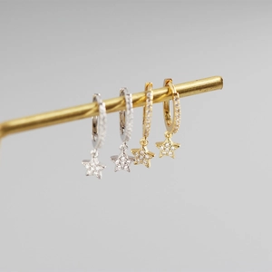 Detail of star-shaped earrings in gold and silver finish with sparkling zircons