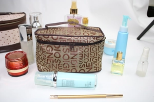Detail of a large brown cosmetic bag with SOIGNE letter pattern and dual zipper closure