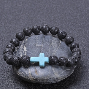 Close-up of black lava stone bead bracelet with a sky blue cross charm on natural rock