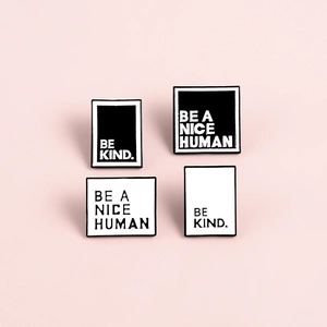 Gros plan de pins en émail noir et blanc minimalistes avec le texte Be A Nice Human sur rose