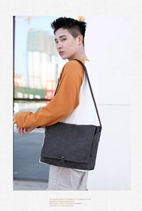Side view of a large charcoal gray canvas messenger bag worn by a model in a city street