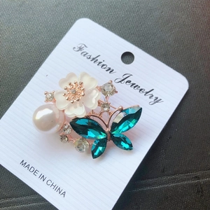 Detail of flower and butterfly brooch with emerald crystals, white petals, and a pearl