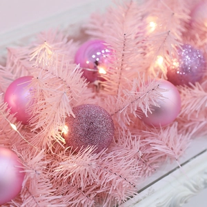 Pink Christmas garland with artificial pine needles, decorative baubles and warm LED lights