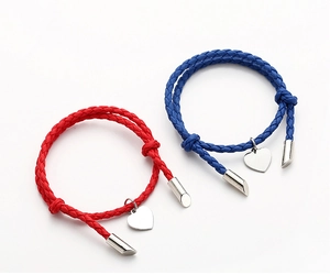 Detail of red and blue braided couple bracelets with metallic heart pendants on white