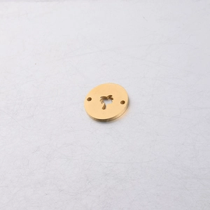 Detail of brass-colored round metal pendant with palm tree cutout and dual holes