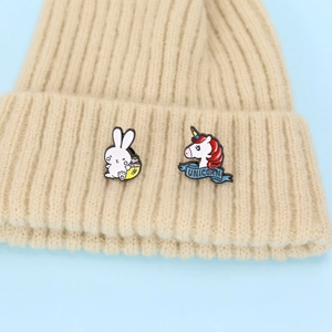 Cute enamel pin set featuring a white bunny and red unicorn on a beige knitted hat