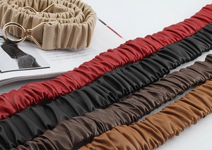 Close-up of five pleated elastic belts with gold metal rings and textured fabric detail