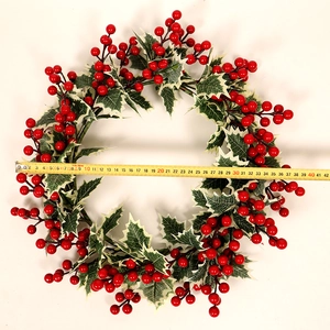 Détail d'une couronne de Noël de 40cm avec baies rouges et feuilles vertes sur fond blanc