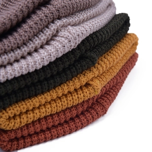 Detail view of thick knit beanie textures in dark grey, green, yellow, and red colors