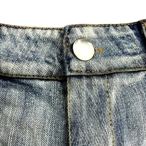 Dettaglio macro di pantaloncini di jeans azzurri con cuciture arancioni e bottone argento