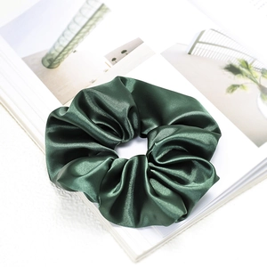 Detailed view of deep green satin silk scrunchie on a clean minimalist magazine page