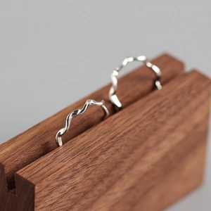 Macro view of minimalist silver wave rings displayed on a premium walnut wood stand