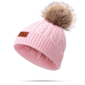 Pink cable knit winter hat for children featuring a fluffy brown faux fur pom-pom topper