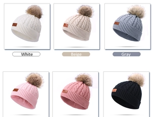 Detail view of cable knit hats in six colors featuring faux fur pom and leather logo tag