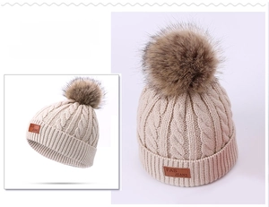 Close-up of cable knit beanie with faux fur pom pom and FAS JEANS leather label detail