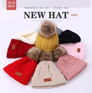Detail of cable knit winter beanies with large fur pom-poms and brown leather labels
