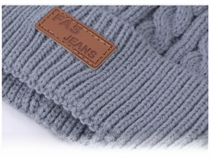 Detail of grey cable knit winter hat featuring a brown leather FAS JEANS logo patch