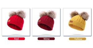 Detail view of cable knit hats in red, wine, and yellow with double fluffy pom-poms