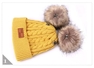 Detail of yellow knit beanie featuring thick cable patterns and dual faux fur pom-poms