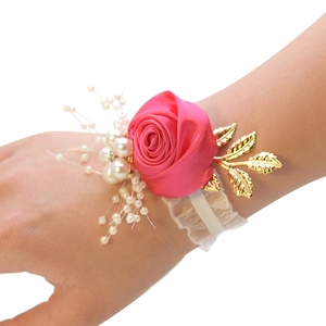 Close-up of pink satin rose wrist corsage with white pearls and gold metal leaves