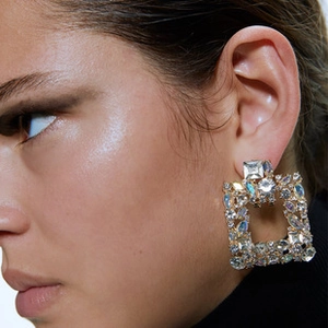 Close-up of golden geometric earrings with colorful sparkling rhinestones on a model