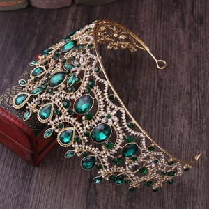 Close-up of golden baroque crown featuring large green gems and sparkling rhinestones