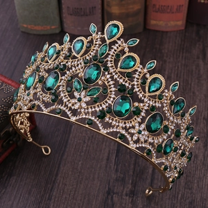 Vintage gold crown with emerald gemstones and rhinestones on dark wooden surface