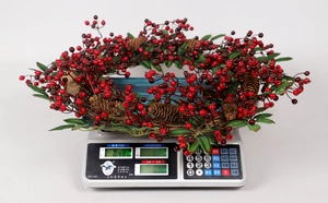 Détail d'une couronne de Noël artisanale avec baies rouges et pommes de pin sur balance
