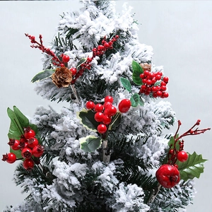 Artificial red berry stems with green leaves and pine cones on snowy Xmas tree
