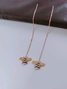 Close-up of titanium tassel earrings featuring a detailed bee motif in rose gold finish