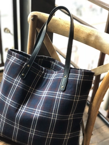 Classic red and navy plaid tote bag with leather strap hanging on a wooden chair