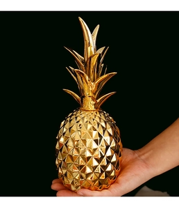 Close-up of hand holding a golden ceramic pineapple decor with metallic electroplated finish