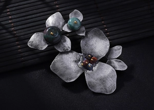 Macro detail of vintage silver flower brooch with natural green stones on dark background