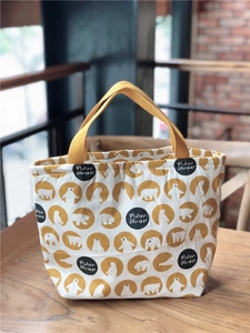 Détail d'un sac à lunch en toile avec imprimé ours polaire et poignées jaunes sur table