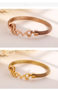 Detail of woven mesh bracelet featuring a love heart charm in gold and rose gold