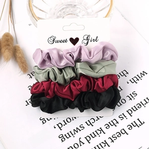Close-up of four satin hair scrunchies in purple, green, red, and black on a card