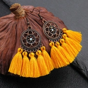 Détail de pompons en coton jaune sur une boucle d'oreille bohème en bronze antique