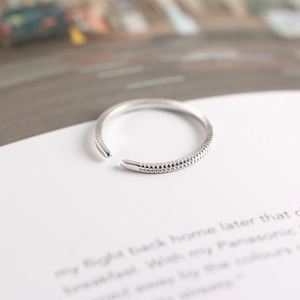 Detail shot of a silver S925 minimalist adjustable ring with striped texture on paper