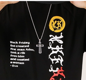 Gros plan d'un pendentif croix argenté porté sur un t-shirt graphique noir pour homme