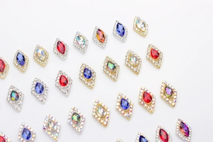 Macro shot of diamond-shaped nail crystals with colorful teardrop stones in gold settings