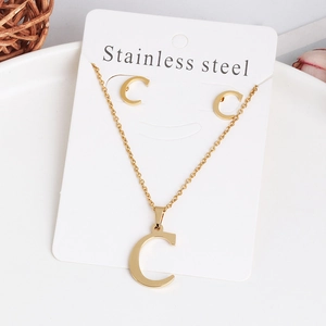 Golden stainless steel letter C pendant necklace and earrings set on white tray
