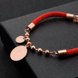 Red braided rope bracelet with rose gold coin and crown charms on leather background