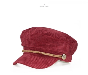 Detail of burgundy corduroy newsboy cap featuring gold braided rope and metal buttons