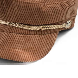 Detail of brown corduroy baker boy hat with golden braided rope and embossed metal button