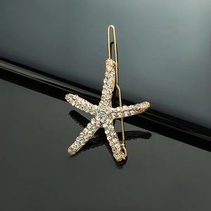 Close-up of a gold starfish hair clip with sparkling white rhinestones on reflective surface