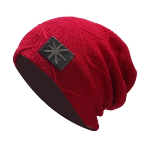 Detail of red cable knit beanie with premium black leather patch and metal star emblem