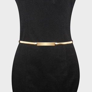 Detail of minimalist gold elastic waist chain with a polished buckle on black dress